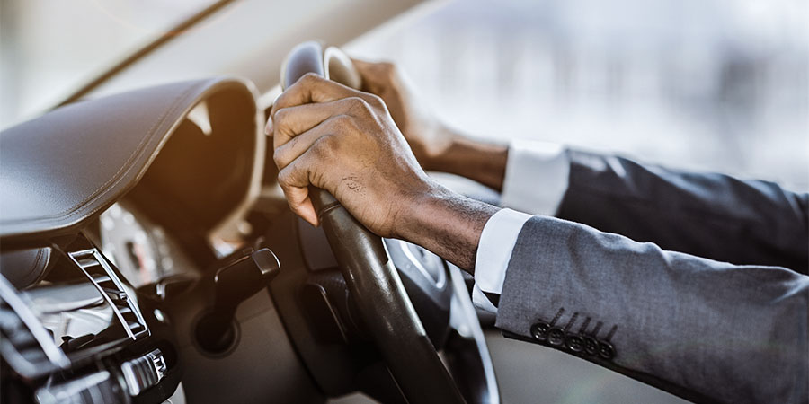 Close up of driver in grey suit holding both hands on steering wheel